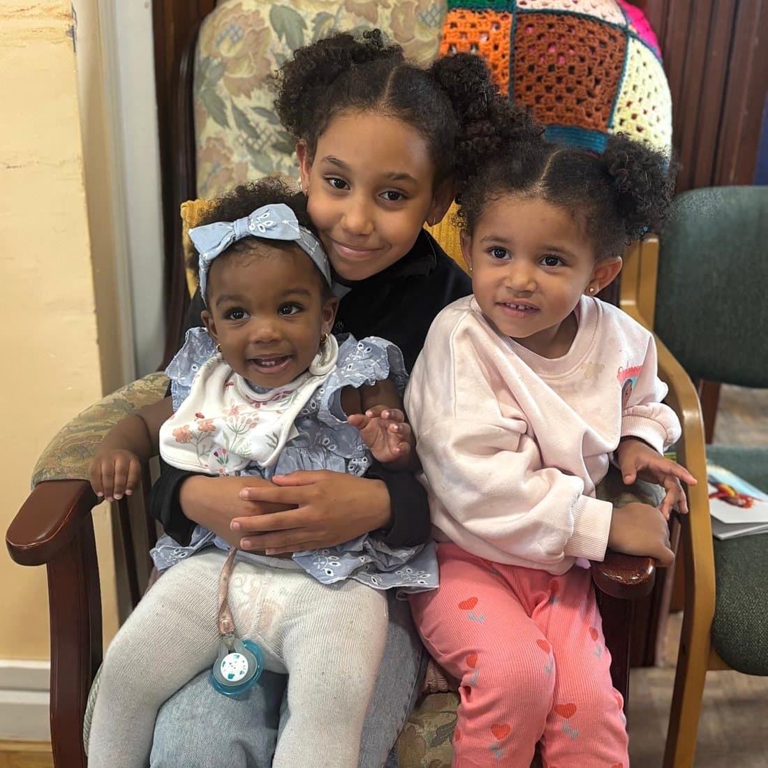 Three smiling little girls sitting together on a chair at church